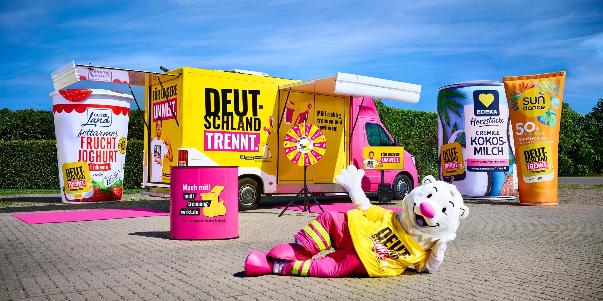Der Trennbär liegt vor dem Show-Truck mit der Aufschrift "Deutschland trennt". Drumherum stehen die XXL-Verpackungen und das Glücksrad.
