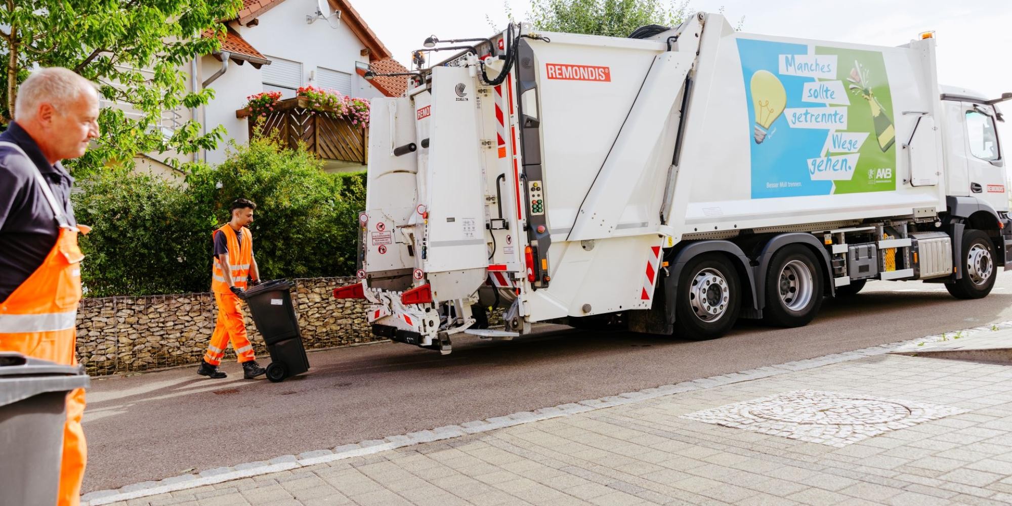 Zwei Müllwerker schieben jeweils eine Mülltonne zum Müllfahrzeug.